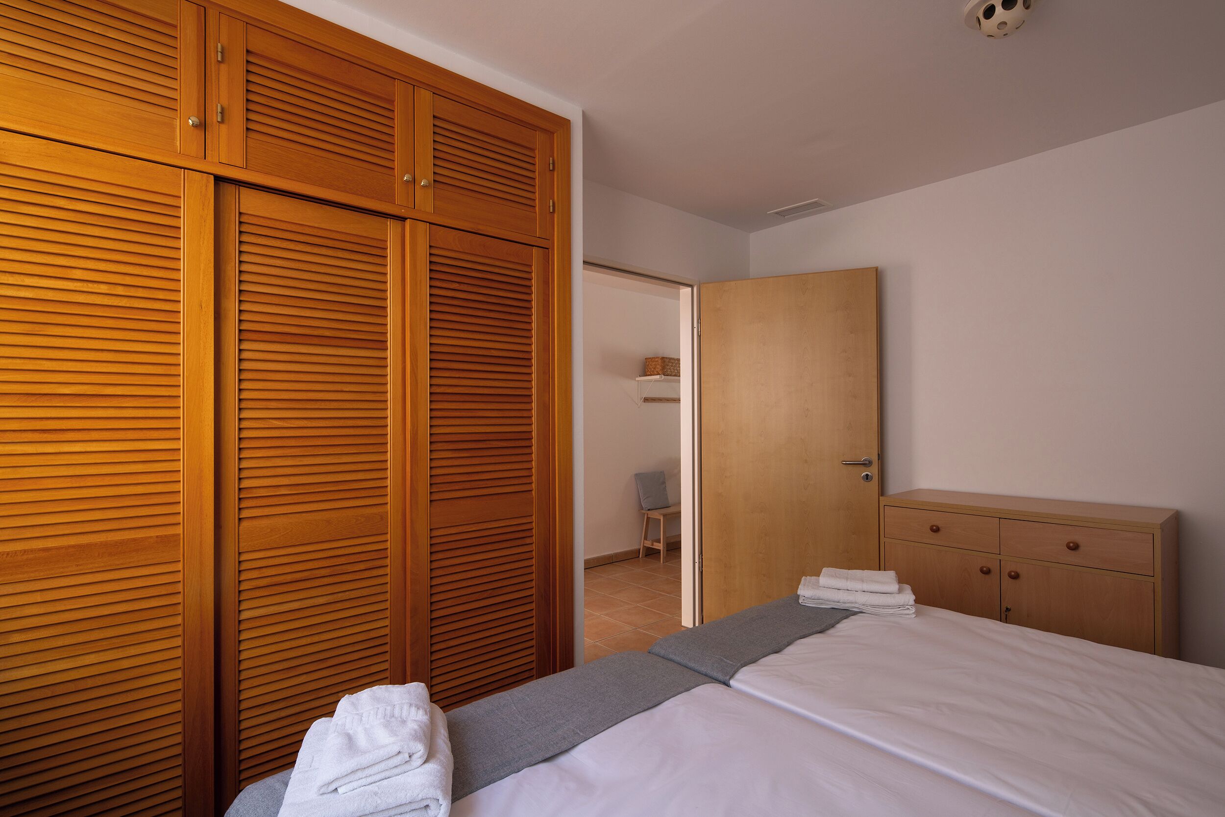 Un dormitorio con cama, armario de madera y escritorio con cajones.