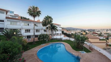 Una piscina de diseño curvo, rodeada por un edificio blanco con balcones y palmeras.