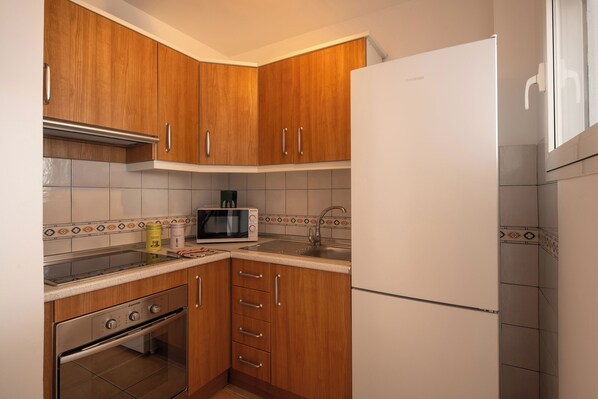 A kitchen with wooden cabinets, a stainless steel oven, a microwave, and a white refrigerator. - APARTAMENTOS TROPICALIA ALMUÑECAR (Almunecar)