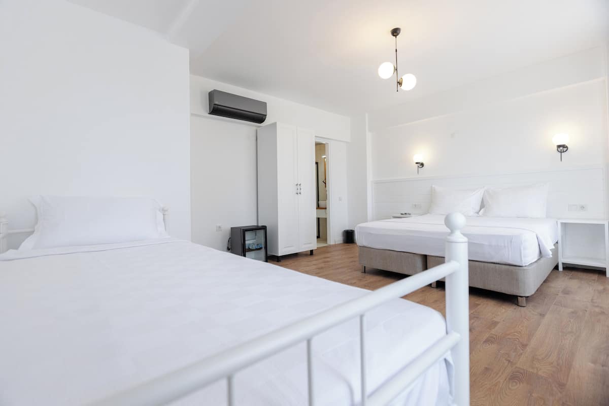 Quarto de hotel com duas camas, um guarda-roupa, uma mesa de cabeceira e um candeeiro no teto.