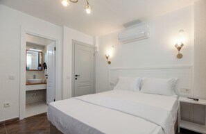A hotel room with a large bed, a bathroom with a sink and mirror, and a ceiling fan. - Karaüzüm Hotel Bozcaada (Bozcaada)