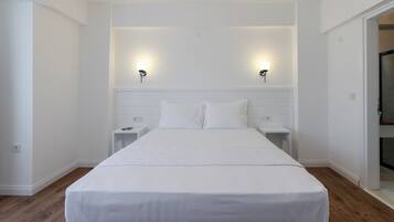 Una cama grande y bien hecha en una habitación con paredes blancas y suelo de madera. Hay dos mesitas de noche con lámparas a ambos lados de la cama.