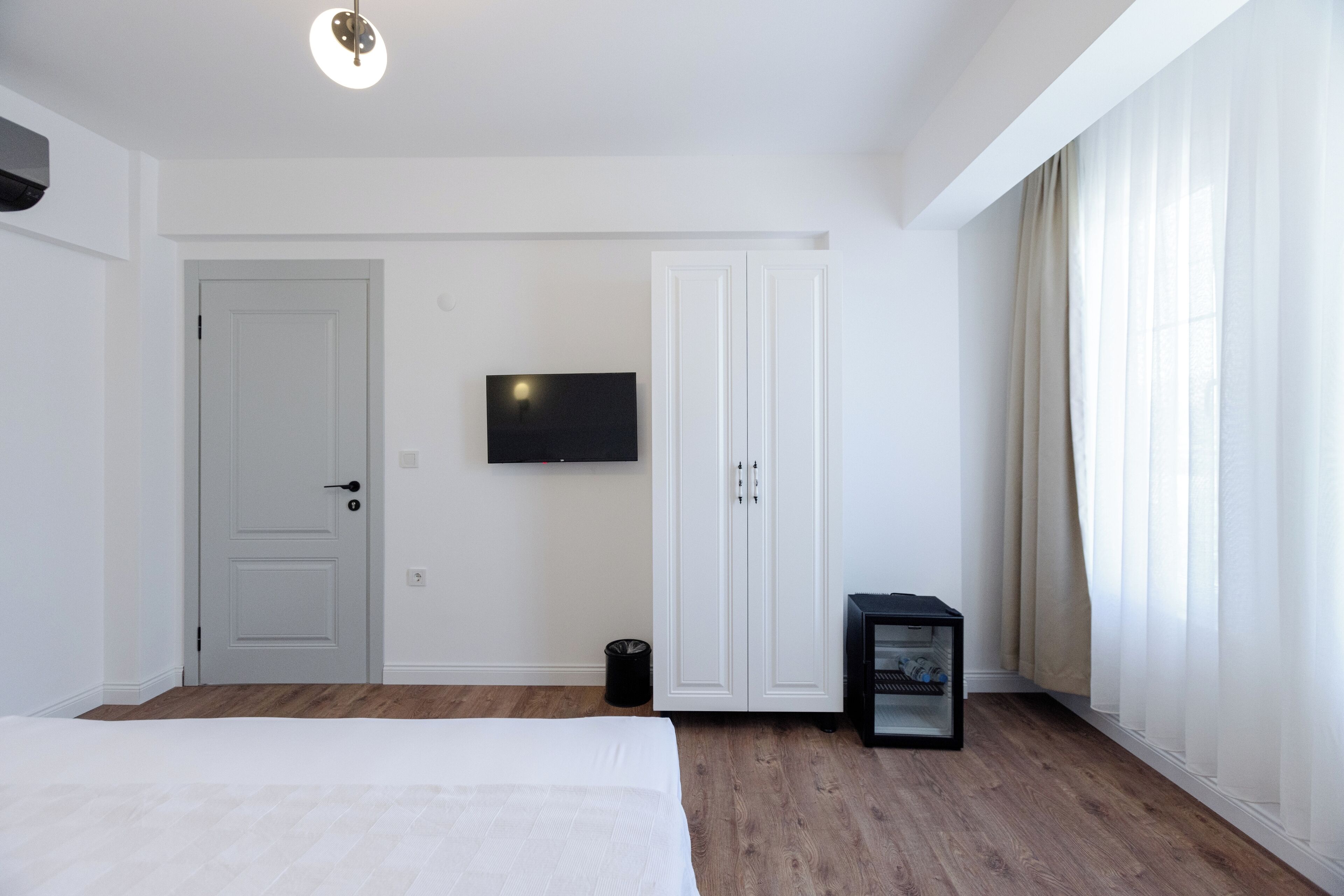 A bedroom with a bed, a TV mounted on the wall, a wardrobe, and a small table with a lamp.