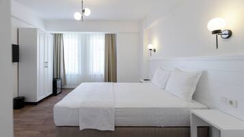 Habitación de hotel con una cama grande, mesitas de noche, un televisor de pantalla plana y vista al pasillo.