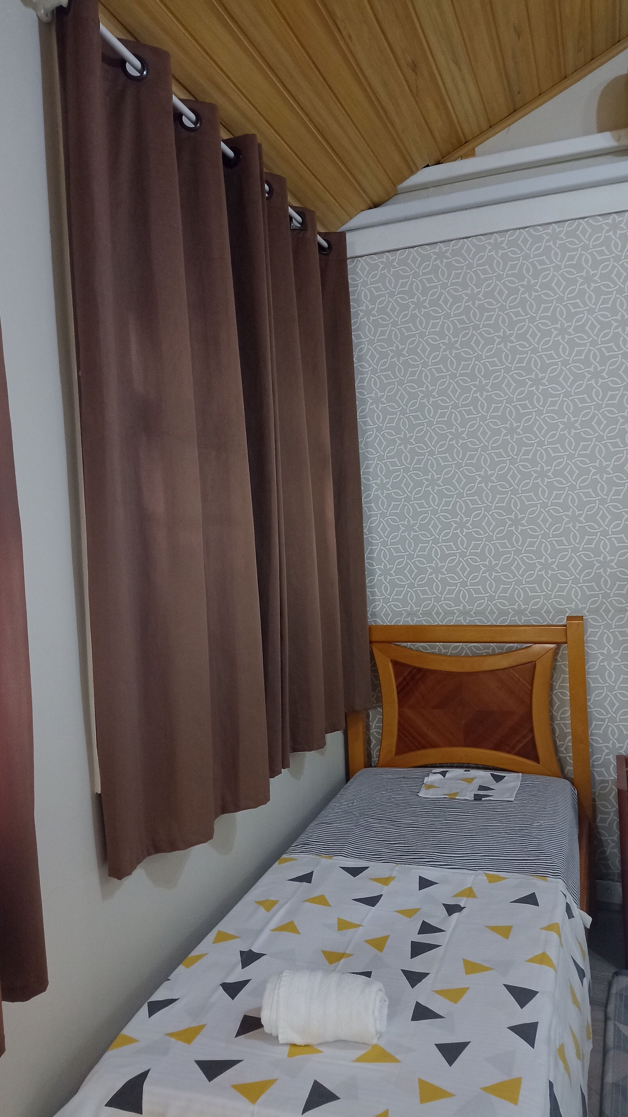 Un lit simple avec une couvre-lit à motifs, une tête de lit en bois et des rideaux marron.