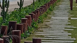 A coastal walkway lined with wooden posts and cacti, leading to a beach with distant mountains. - Mansão de Pirah  (Niteroi)