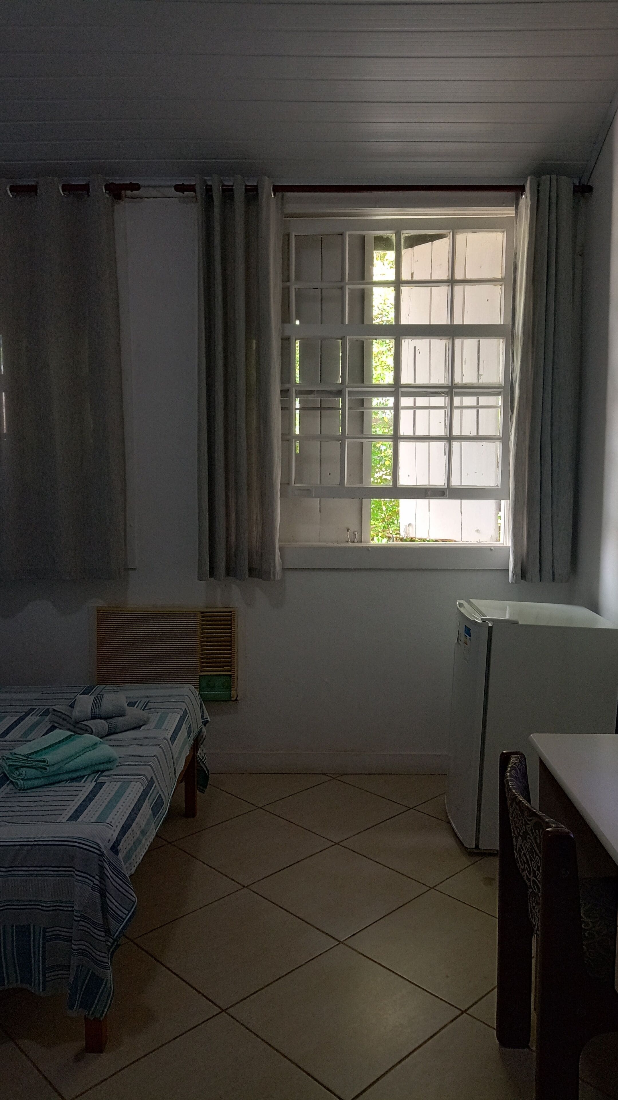 A room with a bed, a desk, a radiator, and a window with curtains.