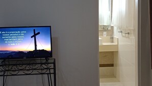 A room with a television displaying a religious message, a tiled floor, and a doorway leading to a bathroom. - Mansão de Pirah  (Niteroi)