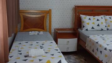 Una habitación pequeña y ordenada con dos camas individuales, una mesita de noche, un armario pequeño, papel tapiz estampado y un aire acondicionado instalado en el techo.