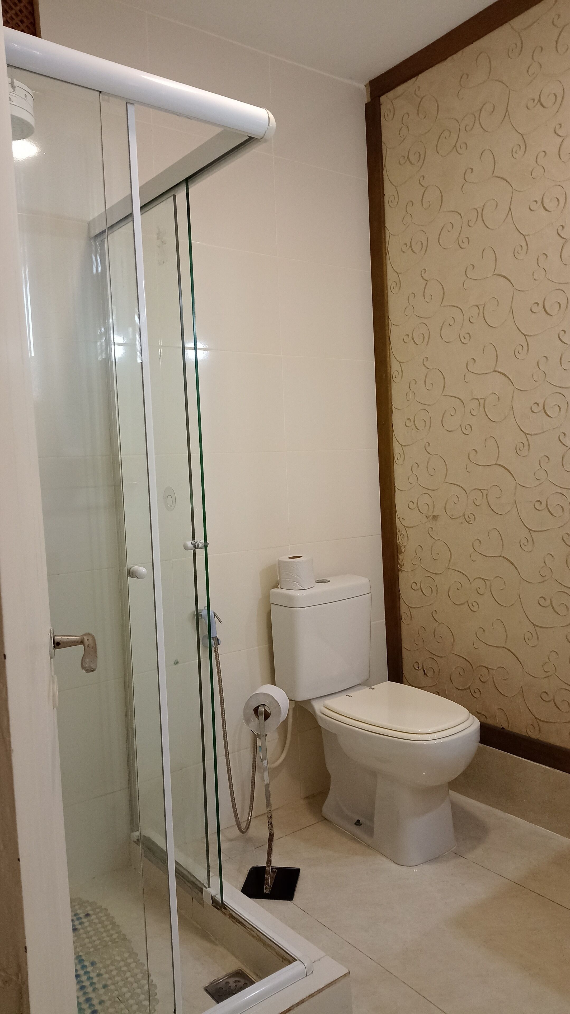 A bathroom with a glass-enclosed shower, a toilet, and patterned wallpaper.