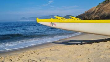 Un kayak con diseño amarillo y blanco sobre una playa con un acantilado rocoso al fondo.