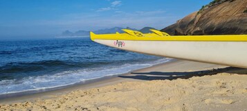 Un kayak con diseño amarillo y blanco sobre una playa con un acantilado rocoso al fondo.