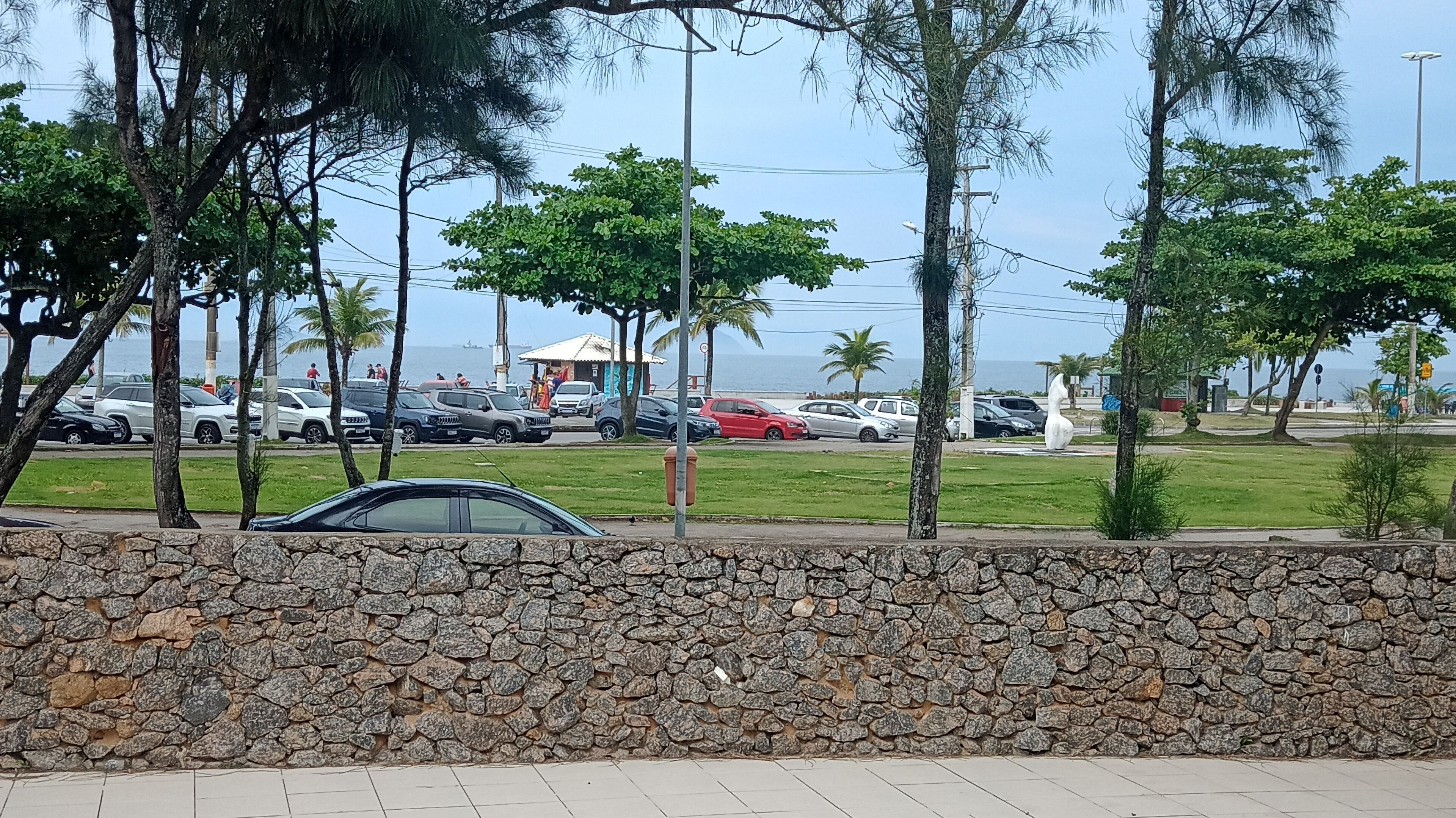 A parking area with a stone wall, parked cars, and trees.