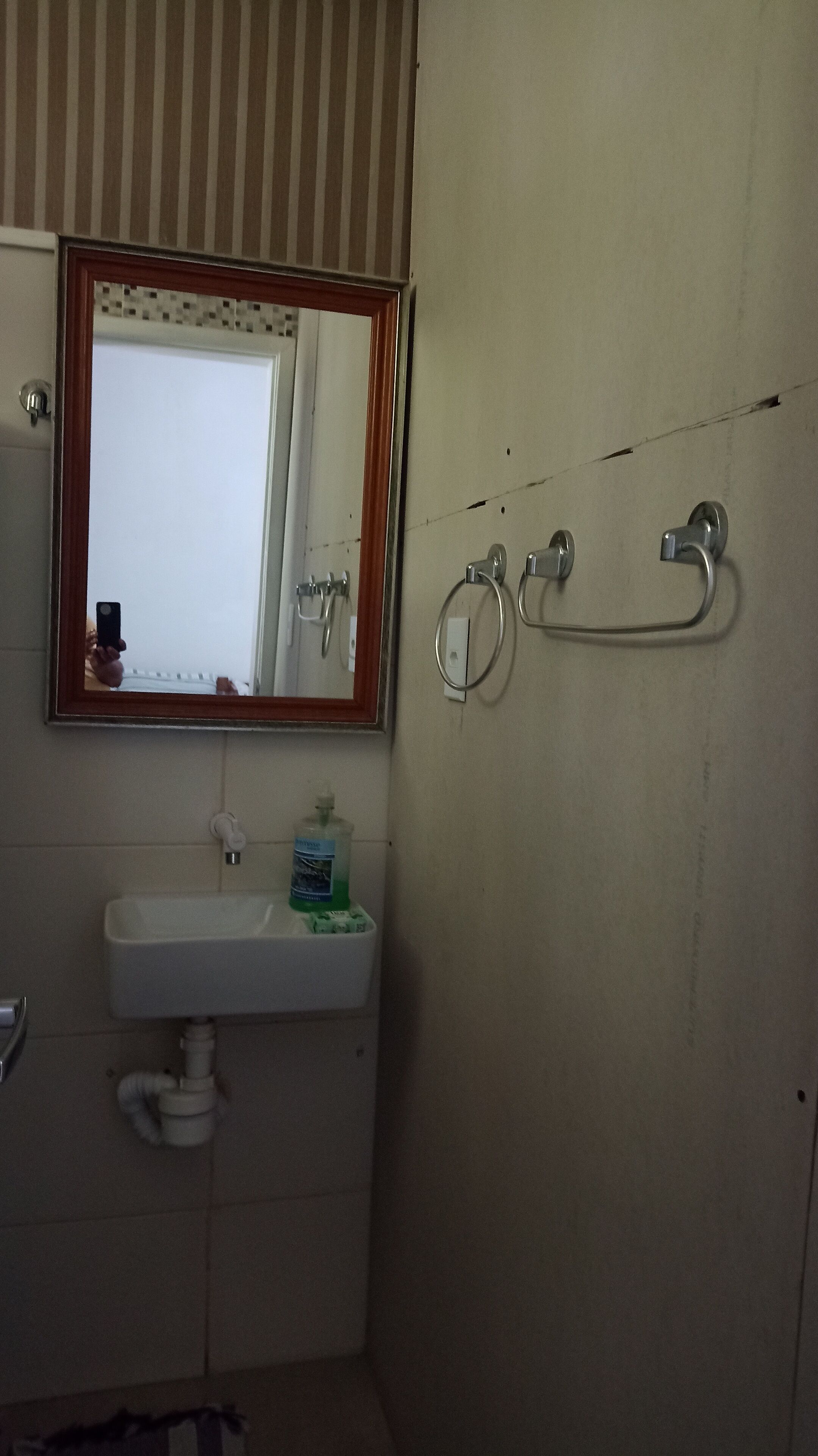 Un baño con lavamanos blanco, espejo con marco de madera y toallero.