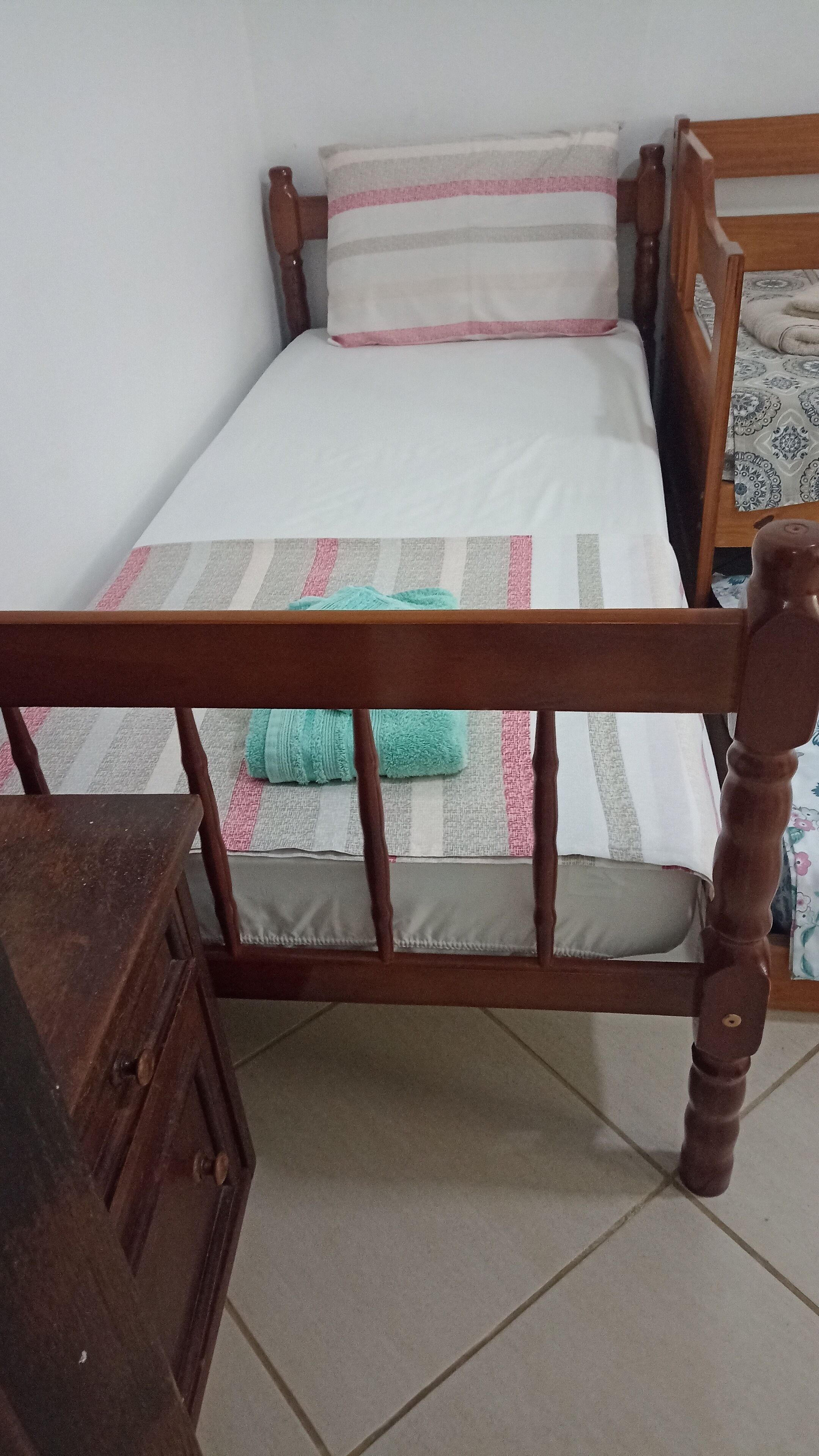 Una cama pequeña y bien hecha, con estructura de madera y colcha a rayas.
