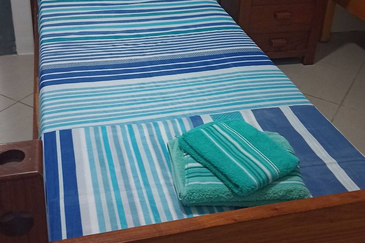 A single bed with a striped bedspread, a wooden headboard, and a wooden nightstand with drawers.