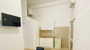 A compact kitchen with white cabinets, a small refrigerator, and a microwave. There is a dining table with two chairs and a remote control on it. - Comfortable and Comfortable as at Home (Acerra)
