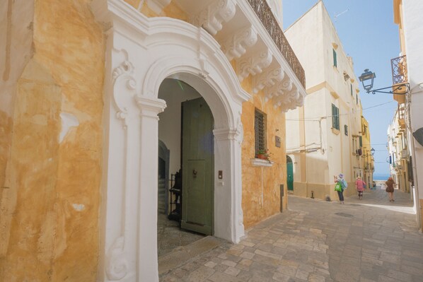 A narrow street with a building featuring an ornate white archway and a green door. - Pascaraymondo Suite Palace (Gallipoli)