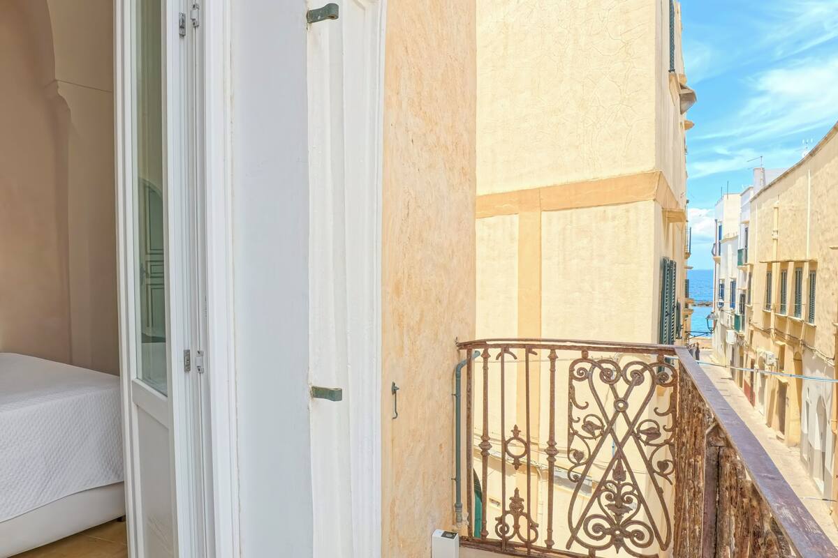 A balcony with a wrought iron railing, a white door, and a view of a coastal street.