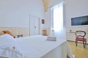 A hotel room with a bed, a chair, a small table, and a window. - Pascaraymondo Suite Palace (Gallipoli)