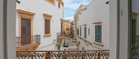 Una calle estrecha con edificios blancos, balcones de rejas de hierro forjado y un cielo despejado.