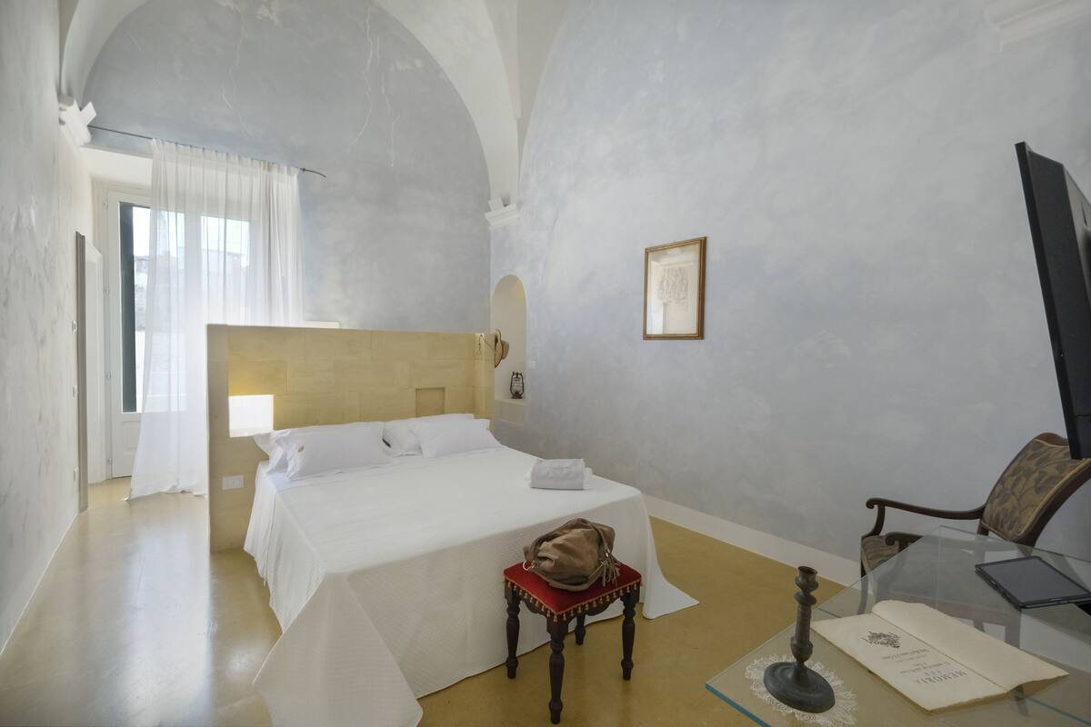 A hotel room with a bed, a chair, a table with a laptop, and a framed picture on the wall.