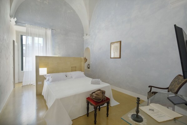 Una habitación de hotel con una cama, una silla, una mesa con una computadora portátil y un cuadro en la pared.