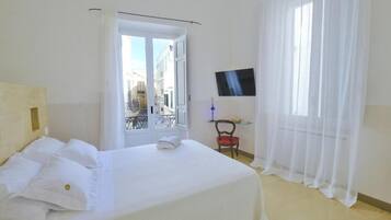 A hotel room with a bed, a TV on the wall, a chair, and a window with curtains.