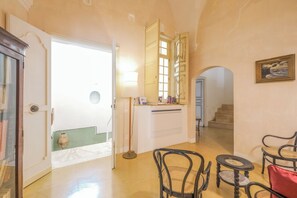 A room with a wooden floor, a white door, a small table with chairs, a lamp, and a painting on the wall. - Pascaraymondo Suite Palace (Gallipoli)