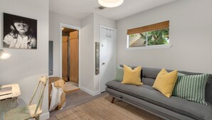 A modern living room with a grey sofa, yellow and green patterned cushions, a wooden chair, a small table, and a framed picture on the wall. - Old Town Retreat w/ Vintage Flair Near Csu, Bikes! (Fort Collins)