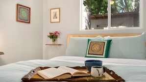 A neatly made bed with a tray holding a book, mug, and bowl, a window with a view of trees, and two framed pictures on the wall. - Old Town Retreat w/ Vintage Flair Near Csu, Bikes! (Fort Collins)