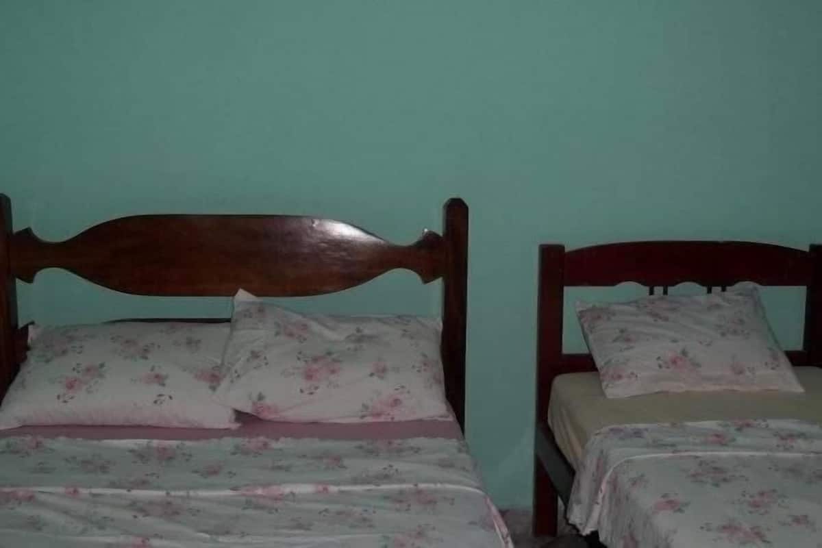A room with two wooden beds against teal walls, each bed has a floral bedspread and matching pillows.