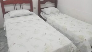 Two single beds with wooden headboards, white bedding with a leaf pattern, and a tiled floor.