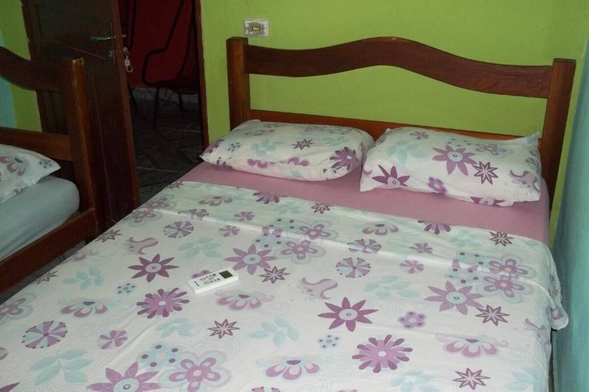 A single bed with a floral-patterned bedspread and two pillows, a wooden headboard, and a red chair in the background.