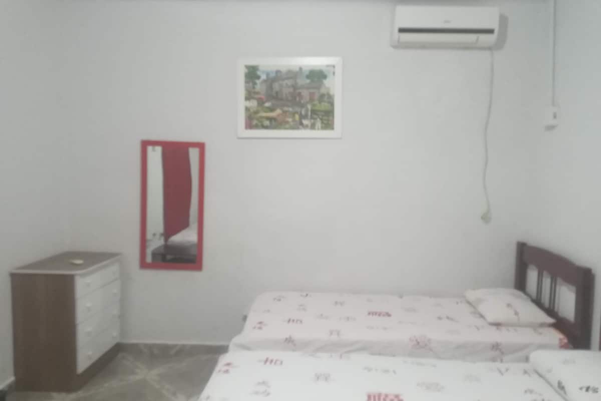 A bedroom with a bed, a dresser, an air conditioner, and a framed picture on the wall.