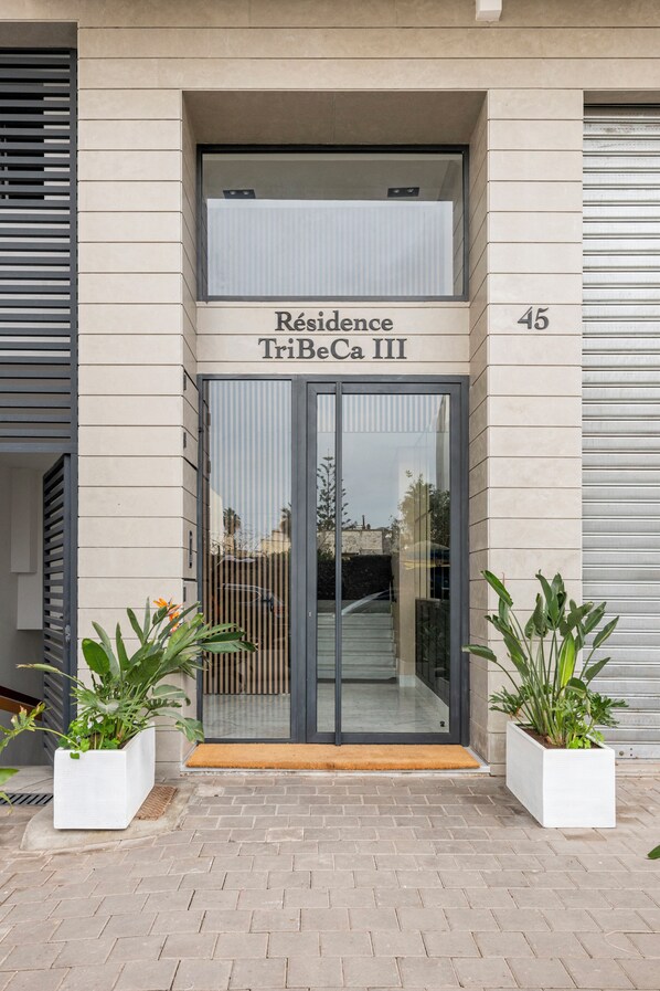 Une entrée moderne d’immeuble avec une porte en verre portant l’inscription « Résidence TriBeCa III » et le numéro « 45 » sur le mur.