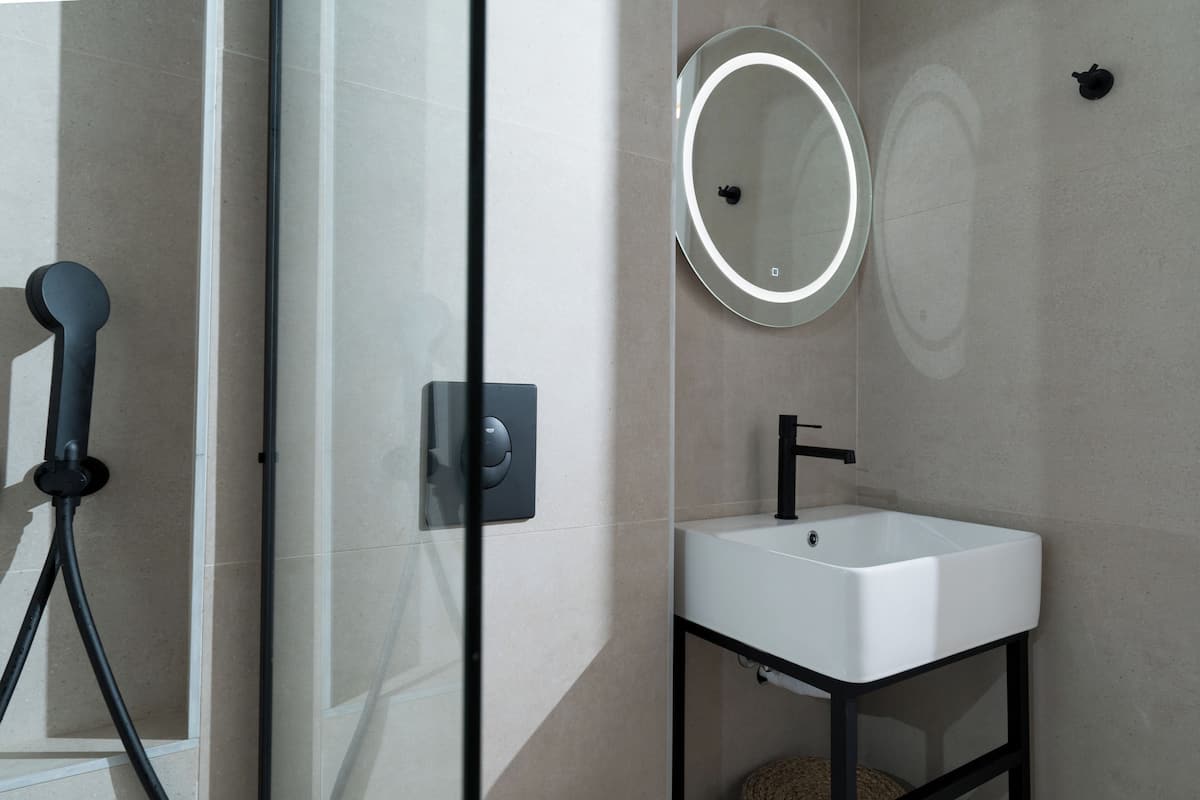 Une salle de bain avec un lavabo blanc, un robinet noir et un miroir rond avec un éclairage intégré.