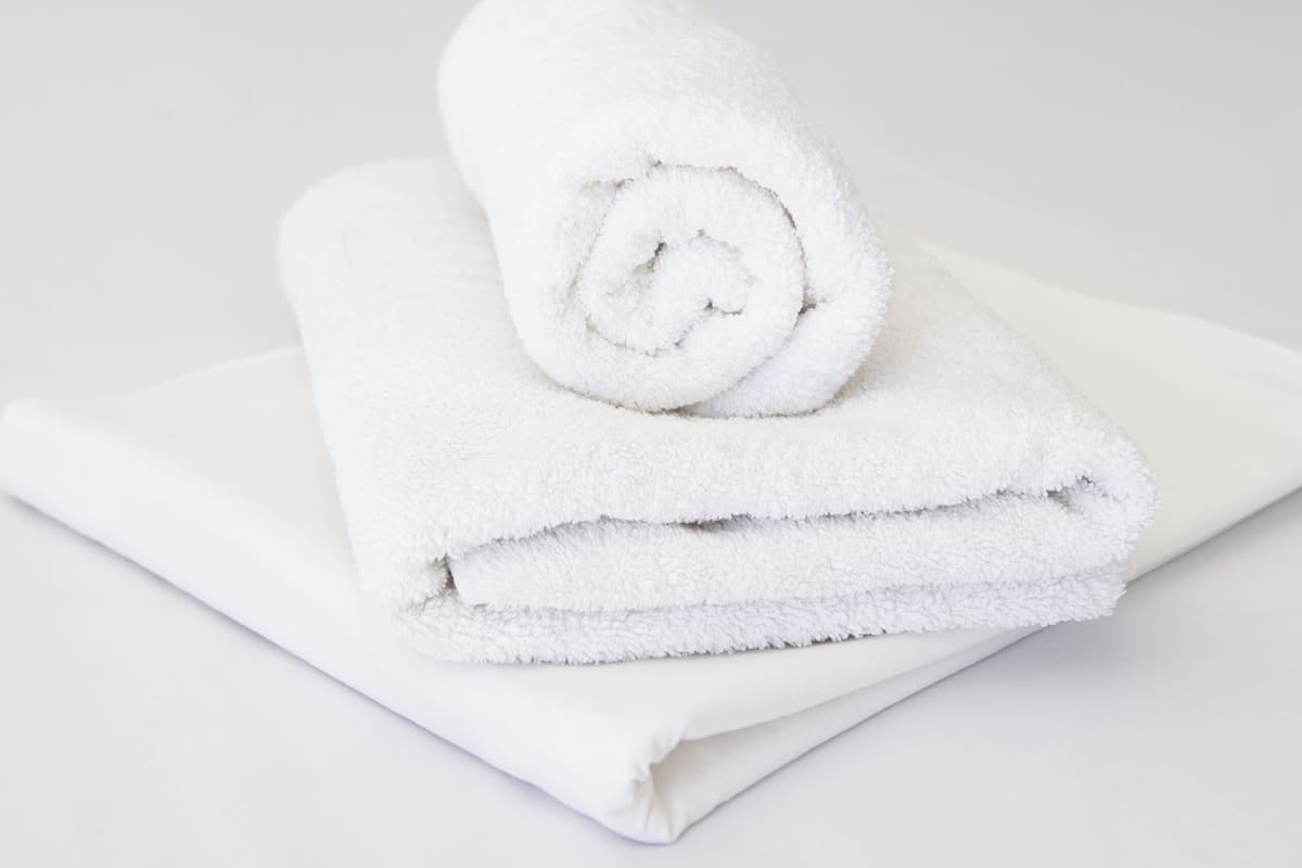 Un lit bien fait, avec des draps blancs et une serviette enroulée posée sur le dessus.