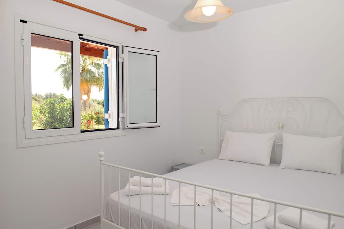 Une chambre à coucher avec un lit, du linge de lit blanc, une fenêtre donnant sur un paysage verdoyant et un luminaire au plafond.