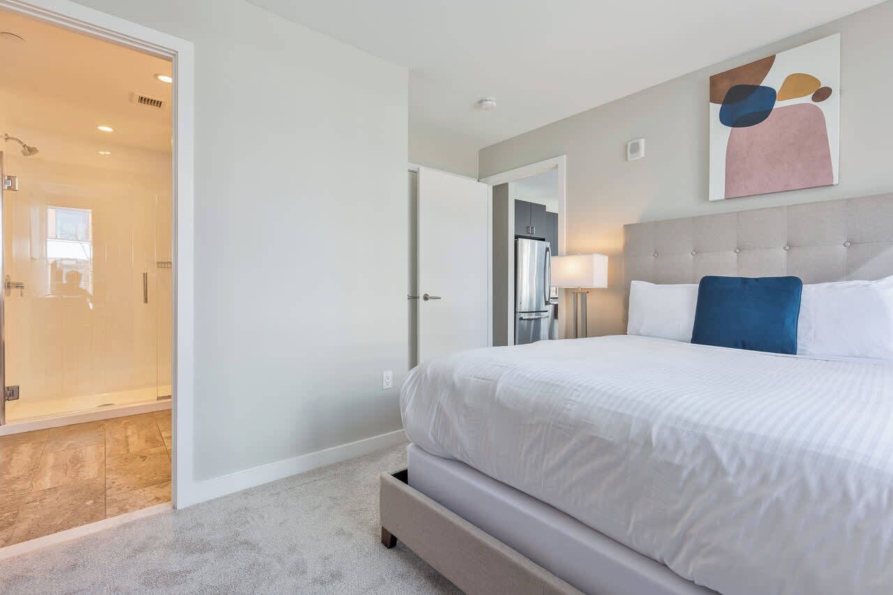 A modern hotel room with a large bed, a walk-in closet, and a bathroom with a glass shower enclosure.