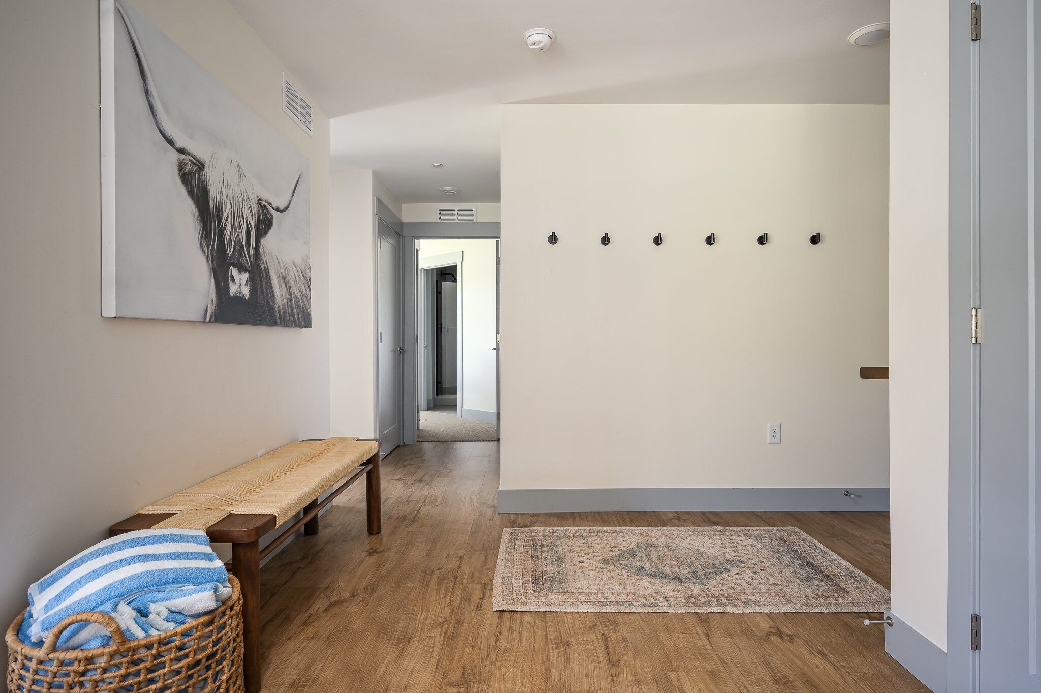 Un pasillo con un banco de madera, una cesta tejida, un tapete y una obra de arte en la pared de un toro.