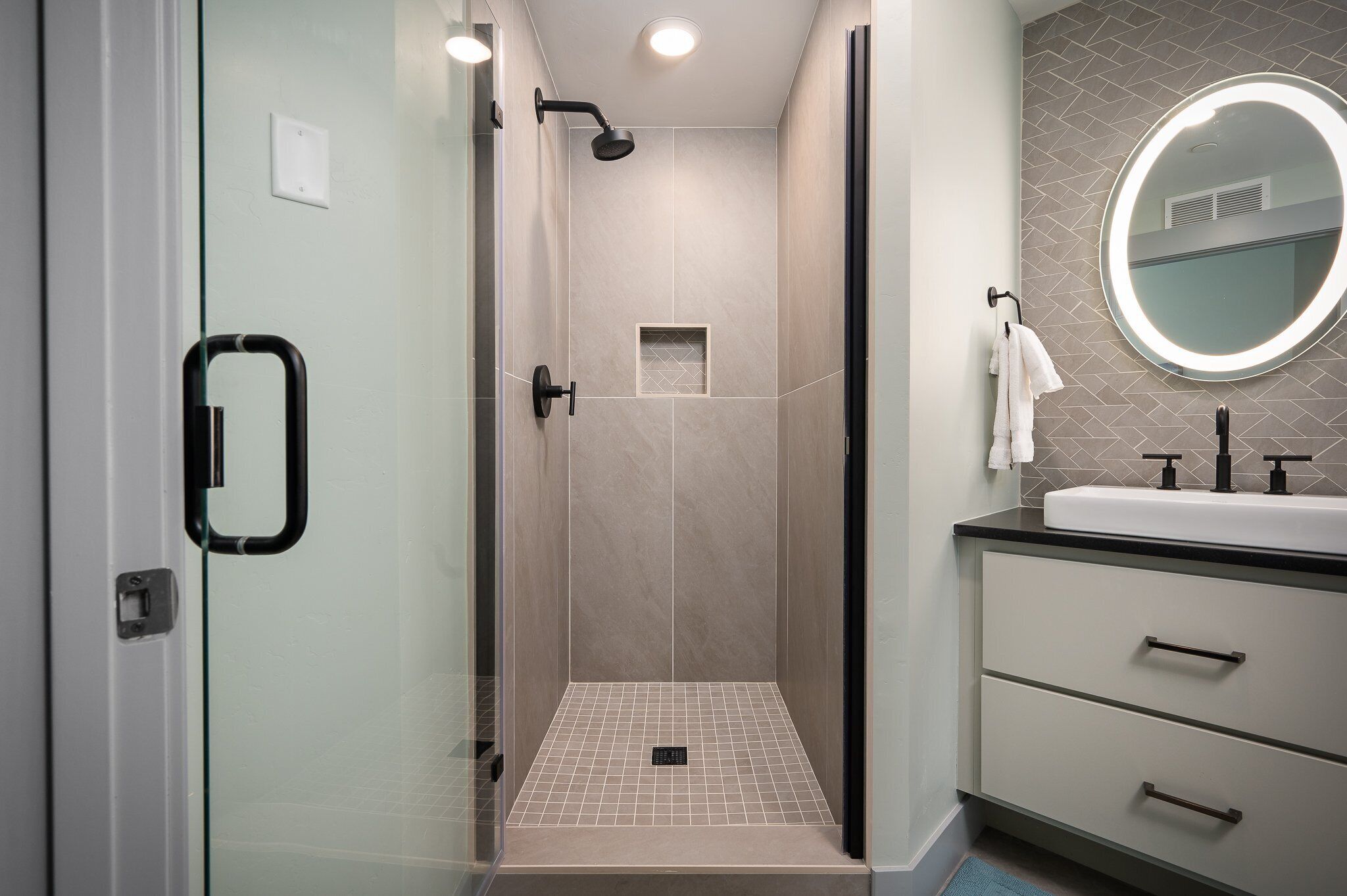 Un bagno moderno con box doccia in vetro, un mobile lavabo e uno specchio con illuminazione integrata.