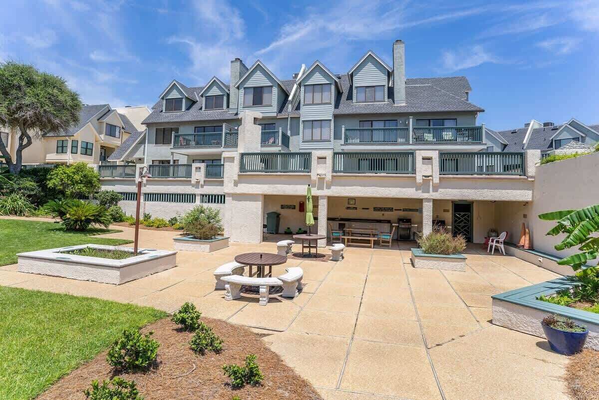 A multi-story residential building with a patio area featuring outdoor furniture and planters.