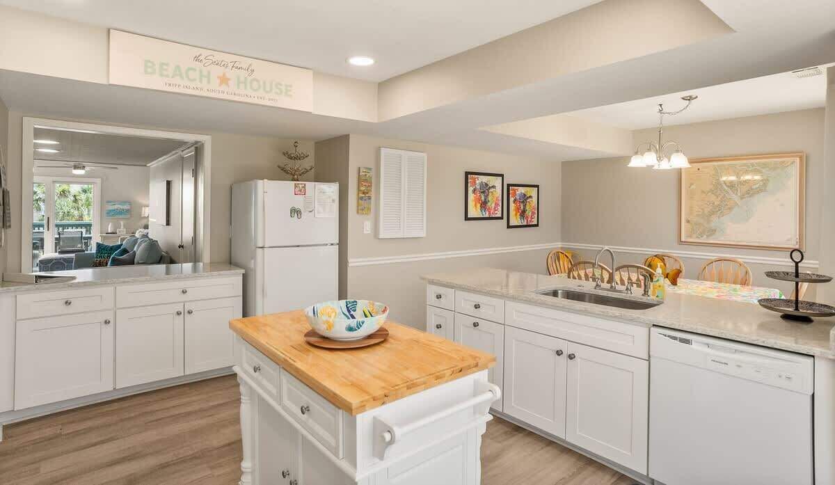 A modern kitchen with white cabinetry, a wooden countertop, a refrigerator, and a dining area with chairs.