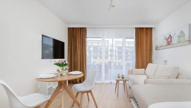 Ein modernes Hotelzimmer mit Essbereich, einer Couch, einem Fernseher und einem großen Fenster mit Vorh ängen.