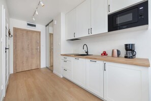 Een moderne keuken met witte kasten, een houten aanrecht, een zwarte magnetron en een koffiezetapparaat.