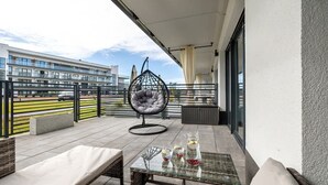 A balcony with a glass table, cushioned seating, and a hanging chair. - Stylish Apartment with Terrace | Spa Access and Parking (Dziwnów)