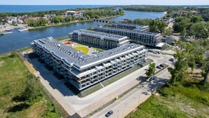 A modern multi-story building with a flat roof, surrounded by greenery and a body of water. - Stylish Apartment with Terrace | Spa Access and Parking (Dziwnów)