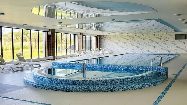 A modern indoor swimming pool with a circular design, surrounded by lounge chairs and a large window offering a view of greenery. - Stylish Apartment with Terrace | Spa Access and Parking (Dziwnów)