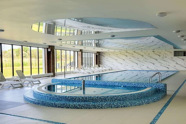The spa area with an indoor pool and circular hot tub by large windows offers luxurious relaxation with a view of greenery.